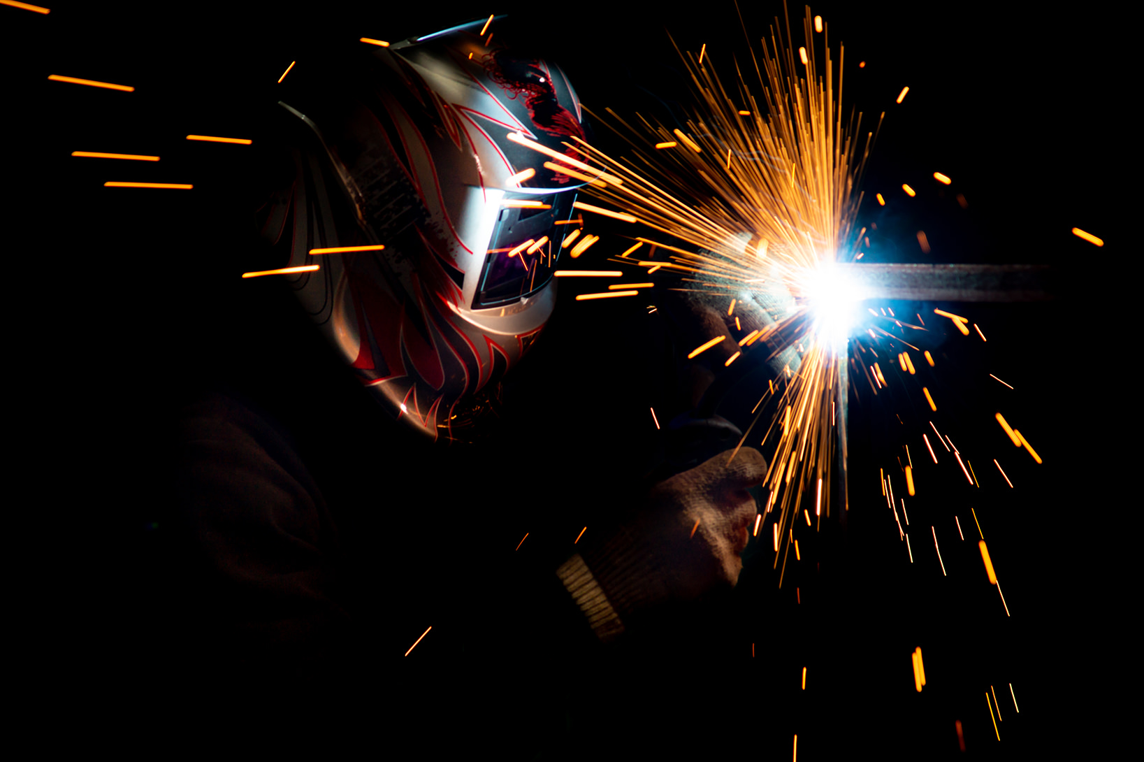 male welder in a mask performing metal welding. photo in dark colors. sparks flying.